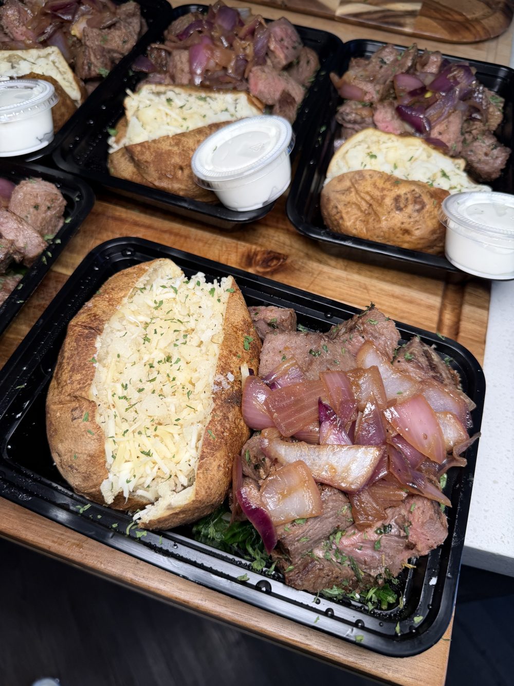 Steak with caramelized onions and a loaded baked potato, portioned in meal containers